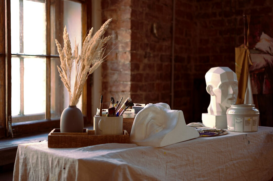 Workshop table with clay, pottery tools and sketchbooks in warm light